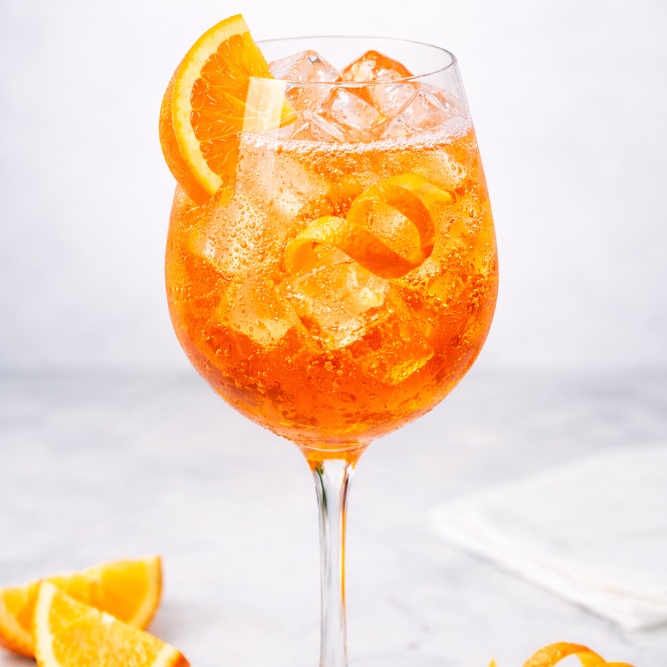 Orange mocktail with ice and orange slices in a wine glass on a white background